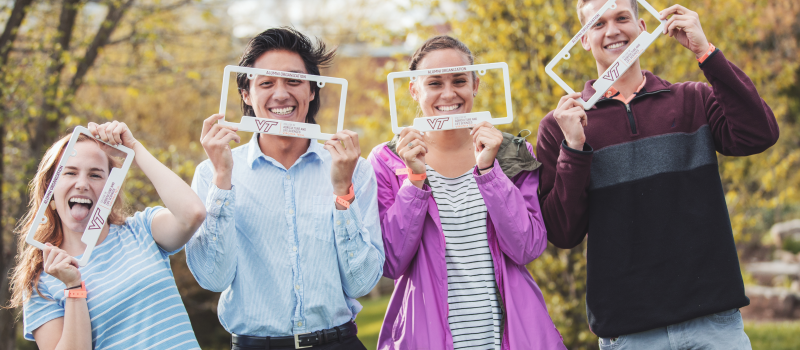 Image of four students smiling and holding license plate holders up to frame their faces.