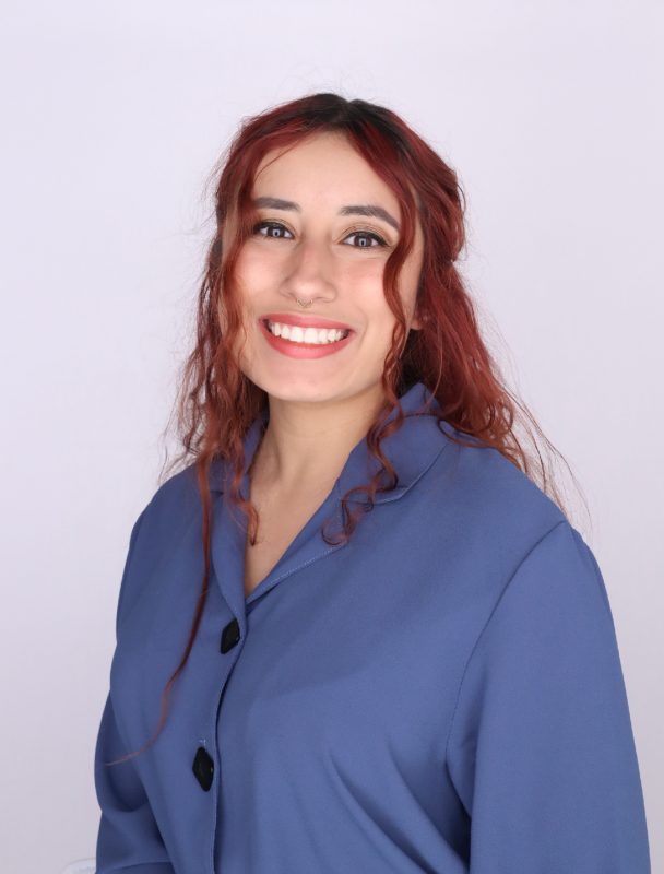 Woman with tan shin and long red hair wearing a blue button-up shirt.