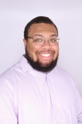 Black man with bear and glasses wearing a pink button up shirt
