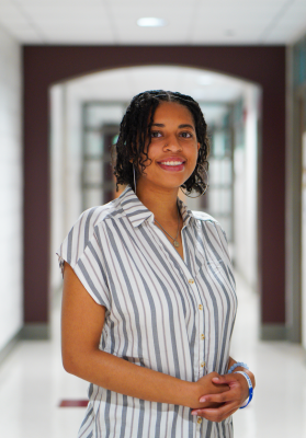 Black woman standing in front of an archway smiling and wearing a striped shirt.