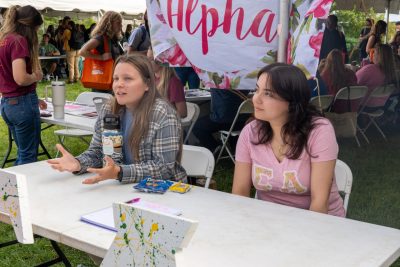 Two females sitting in their booth and talking to another student