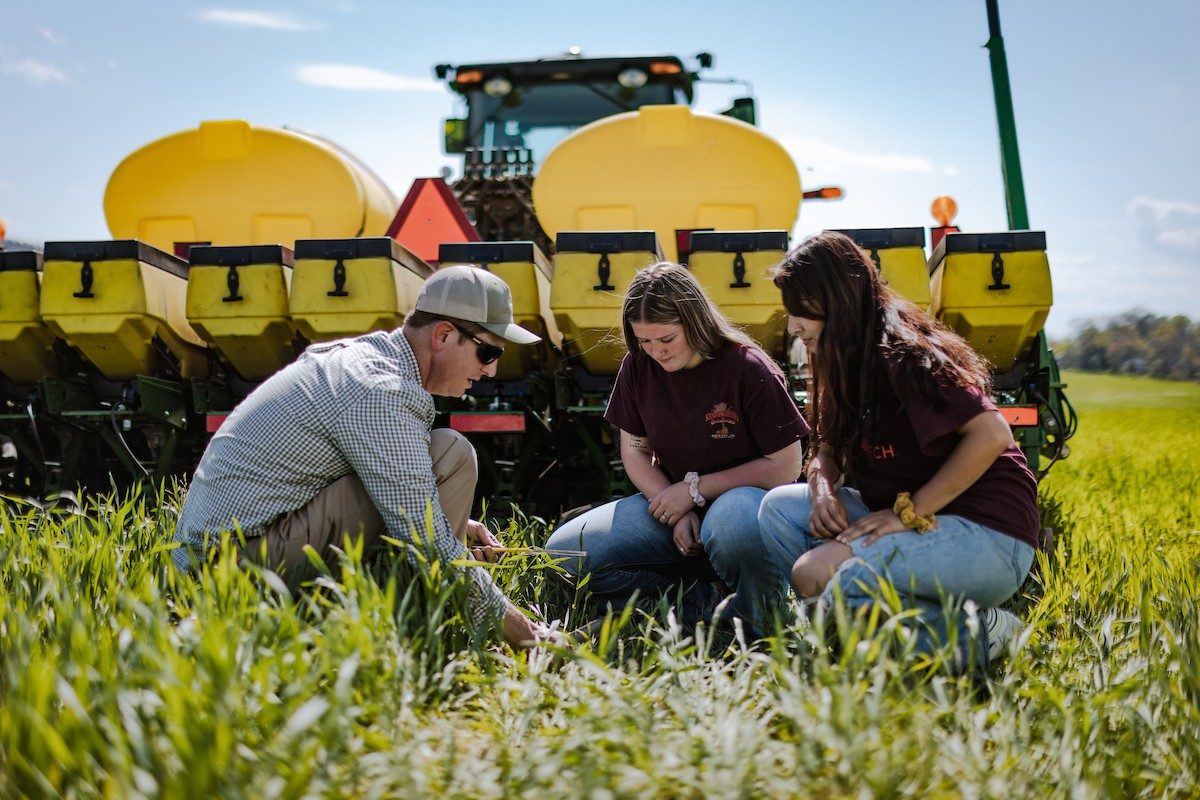 Students and instructor checking corn seed depth behind a planter in a field.
