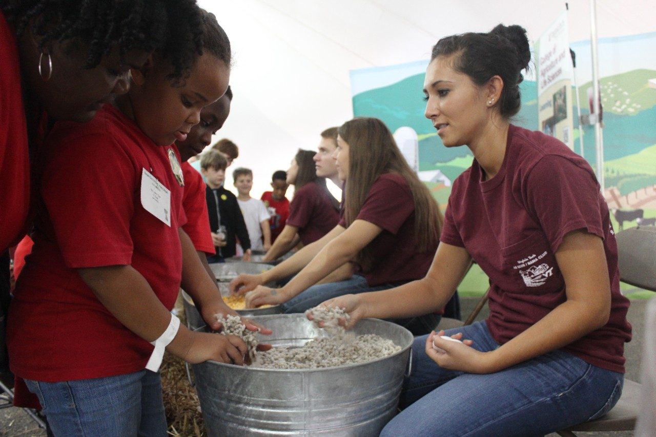 A student works at a state fair with a child from the community.