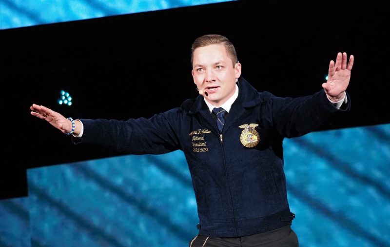 Andrew Seibel spreads his hands in a wide gesture while speaking on stage.