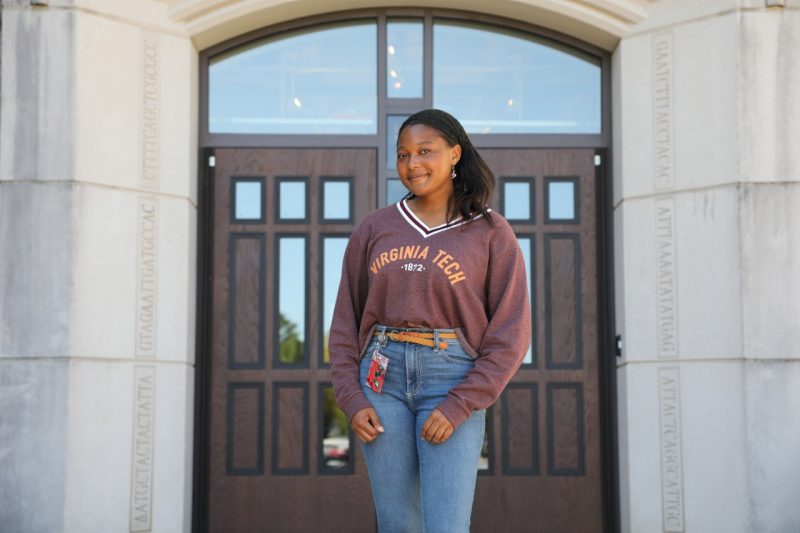 A woman in a Virginia Tech sweatshirt stands in front of a campus building.