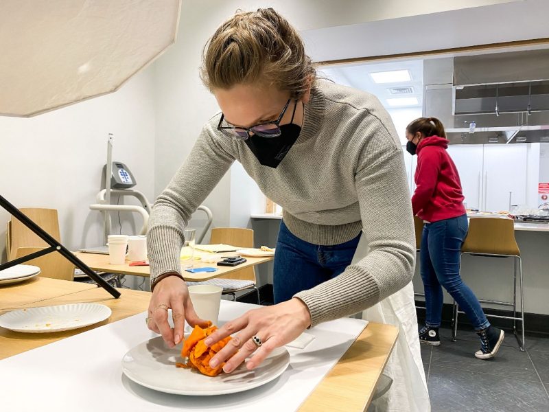 Woman in tan sweater places food on a plate.