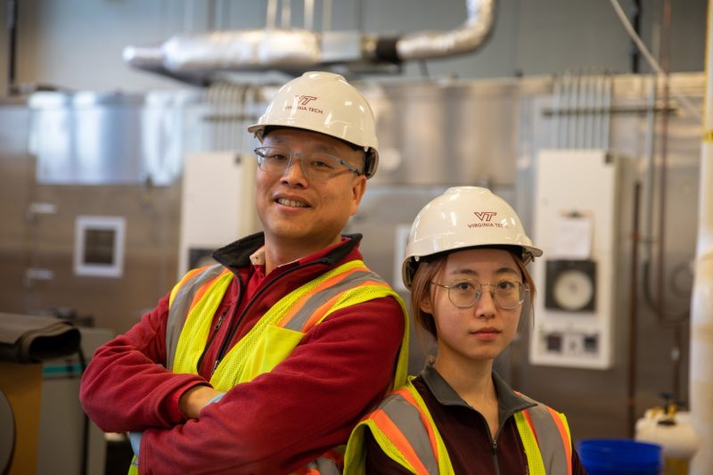 A man and woman in yellow vests are hard hats in a lab.